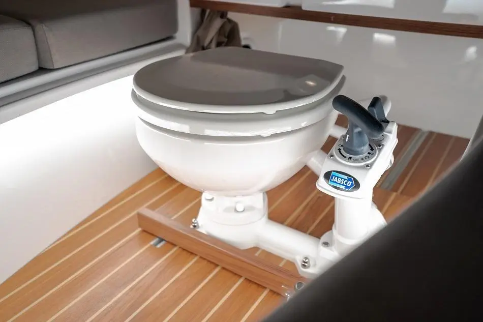 Marine toilet with Jabsco branding, mounted on wooden floorboard in a modern boat interior.